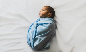 Swaddled newborn sleeping soundly using soothing techniques from this baby sleep guide.