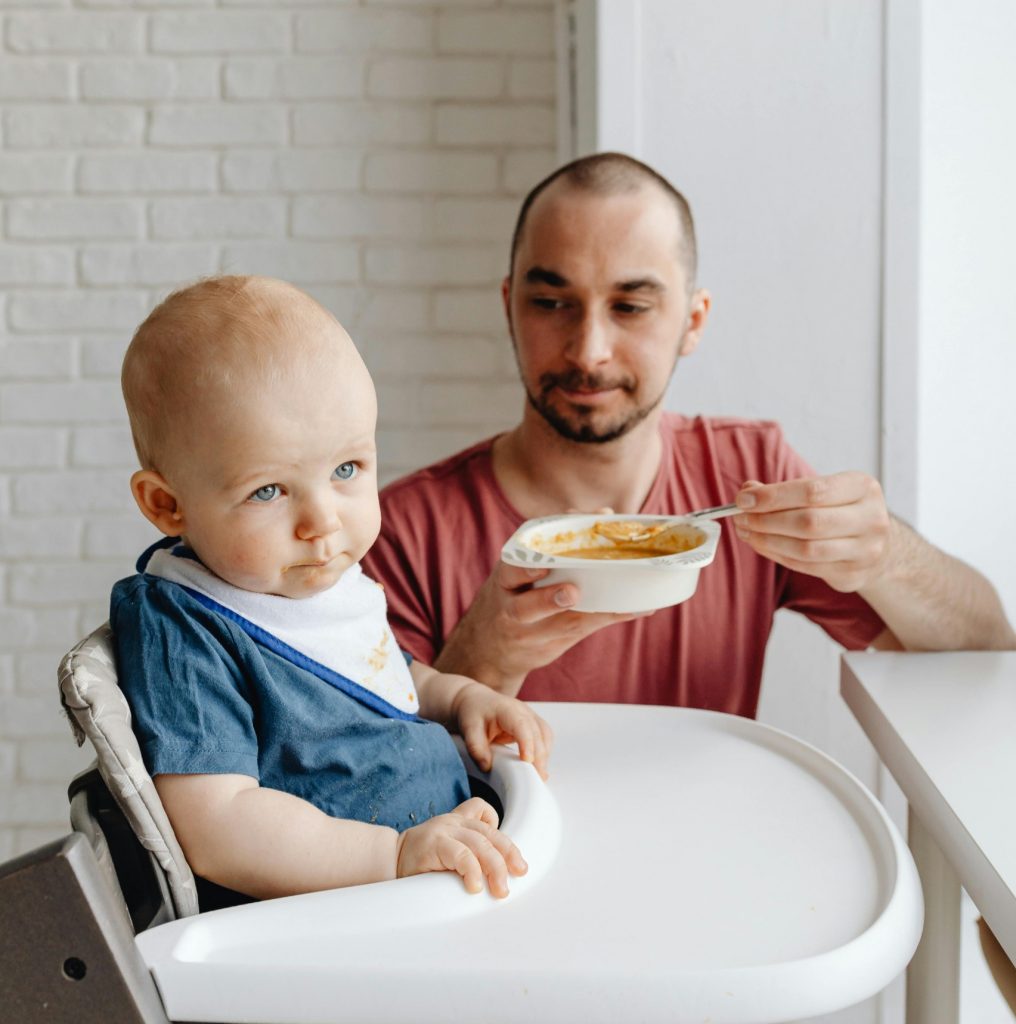 parent gently encouraging toddler to eat while child resists
