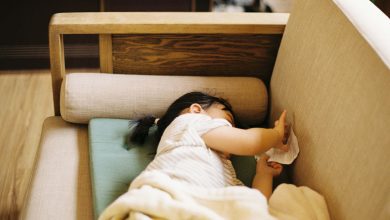 A toddler napping on a sofa chair during a trip, showing a flexible approach to baby sleep in a hotel or Airbnb.