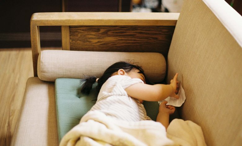 A toddler napping on a sofa chair during a trip, showing a flexible approach to baby sleep in a hotel or Airbnb.