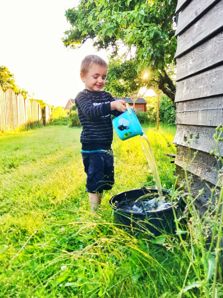 Toddler pouring water between cups at a simple backyard water play station