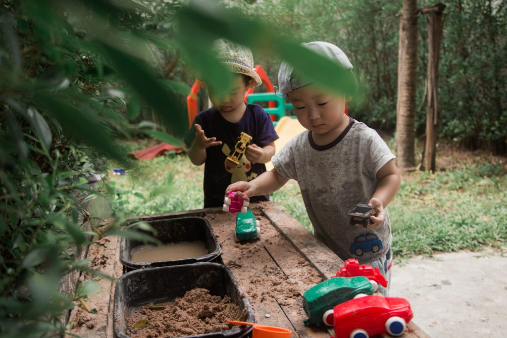 toddler enjoying imaginative outdoor pretend play with a mud kitchen