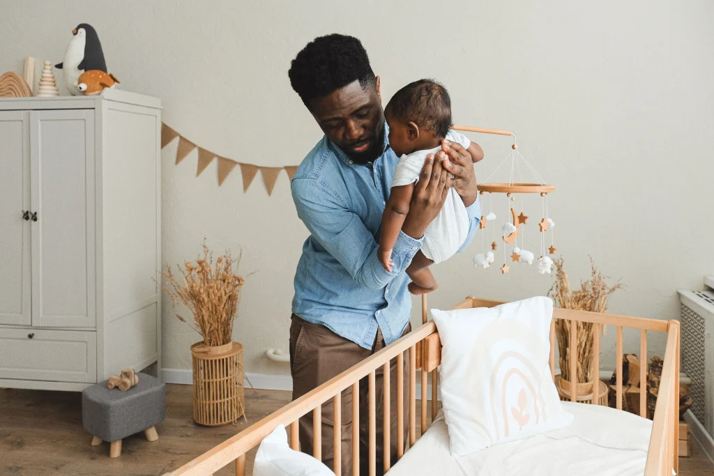Parent gently lowers a sleeping baby onto their back in an empty crib
