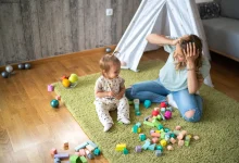 toddler playing with blocks while mother looks on in a relatable parenting moment